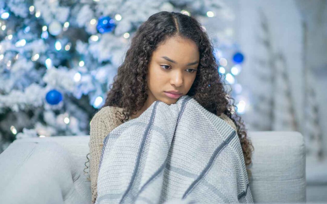 A lonely girl of african descent cuddles under a blanket by herself. She is sad and depressed to be by herself for the holidays. Seasonal Affective Disorder.